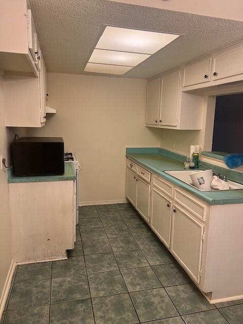 kitchen featuring dark tile patterned flooring, white cabinetry, and sink