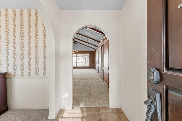 hall featuring a textured ceiling, lofted ceiling with beams, and light colored carpet