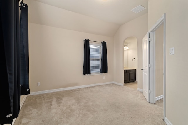 unfurnished bedroom with connected bathroom, light colored carpet, and lofted ceiling