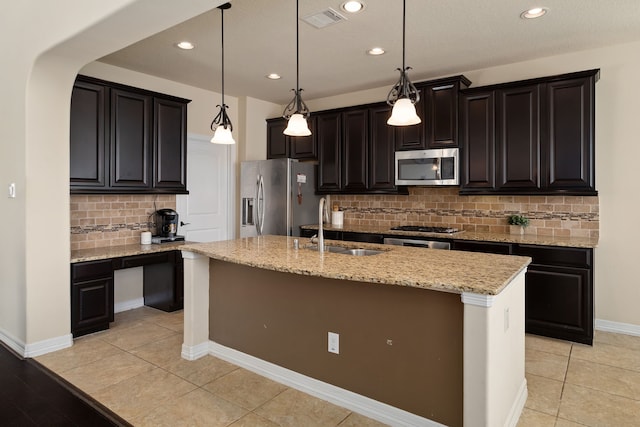 kitchen featuring a kitchen island with sink, sink, stainless steel appliances, and hanging light fixtures