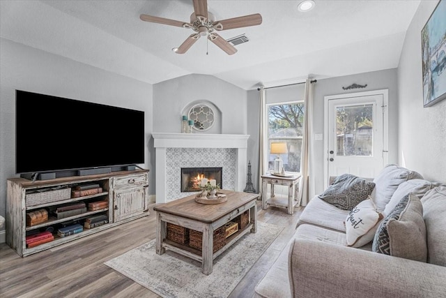 living room with ceiling fan, hardwood / wood-style floors, a textured ceiling, vaulted ceiling, and a tiled fireplace