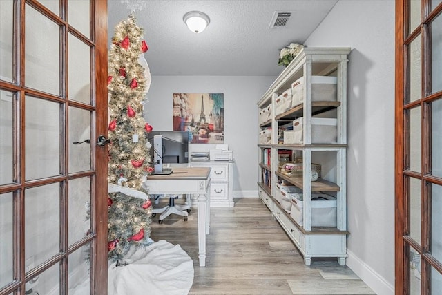 home office with french doors, light hardwood / wood-style flooring, and a textured ceiling