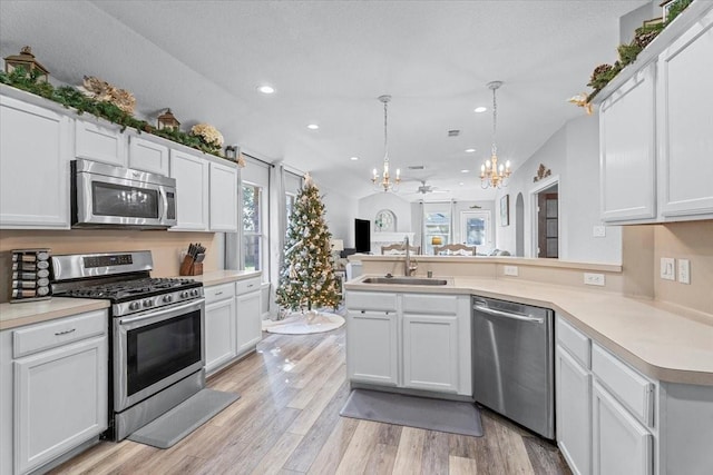 kitchen with appliances with stainless steel finishes, ceiling fan with notable chandelier, sink, white cabinets, and hanging light fixtures