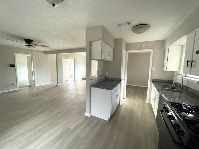 kitchen featuring light hardwood / wood-style floors, ceiling fan, sink, stainless steel stove, and white cabinetry