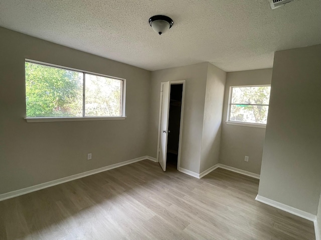 unfurnished bedroom with multiple windows, a textured ceiling, light hardwood / wood-style floors, and a closet