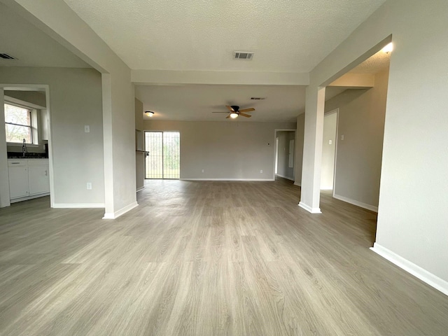 unfurnished living room with ceiling fan, sink, a textured ceiling, and light hardwood / wood-style flooring