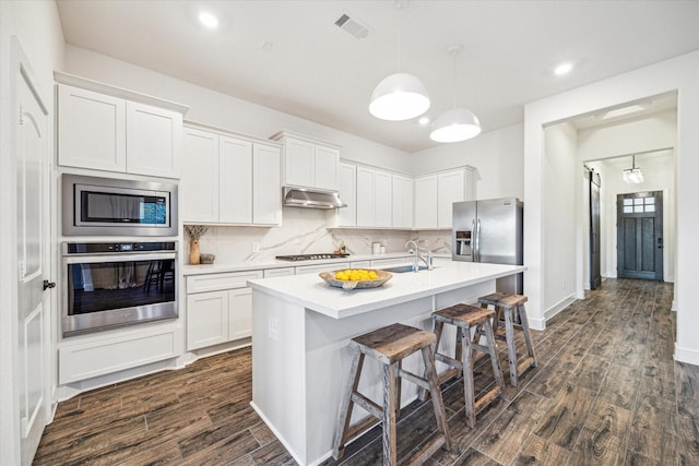 kitchen with stainless steel appliances, white cabinetry, and an island with sink