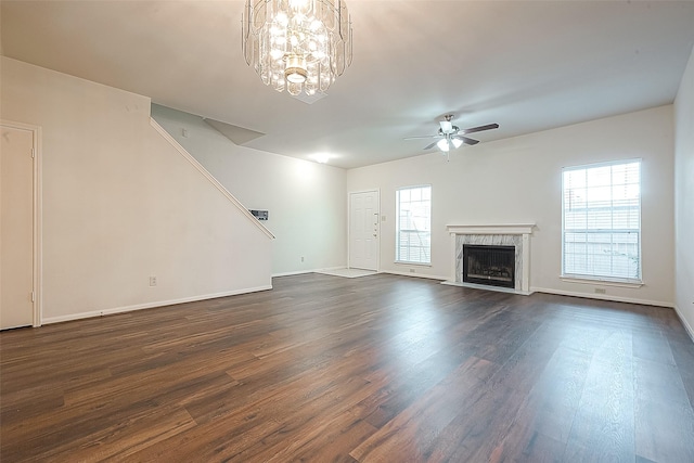 unfurnished living room featuring ceiling fan with notable chandelier, dark hardwood / wood-style floors, a fireplace, and a wealth of natural light