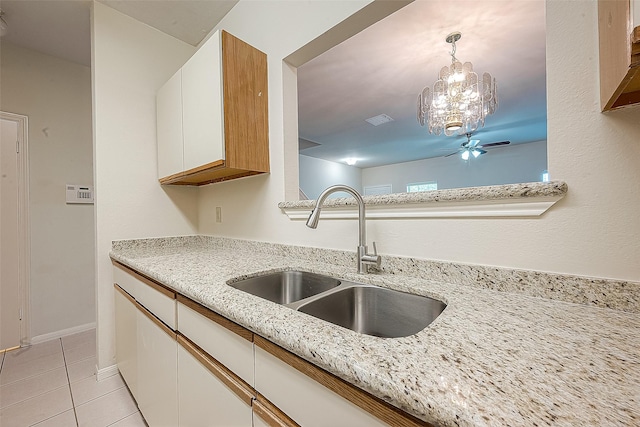 kitchen with light stone countertops, sink, decorative light fixtures, white cabinetry, and light tile patterned flooring