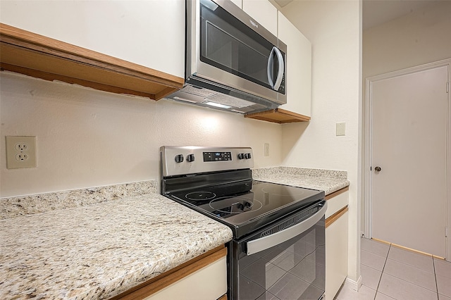 kitchen featuring light tile patterned floors, white cabinetry, light stone counters, and appliances with stainless steel finishes