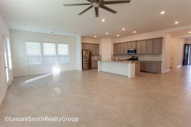 kitchen with a kitchen island with sink, sink, ceiling fan, light stone counters, and stainless steel appliances