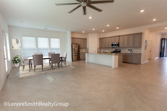 kitchen with ceiling fan, sink, light stone countertops, an island with sink, and appliances with stainless steel finishes