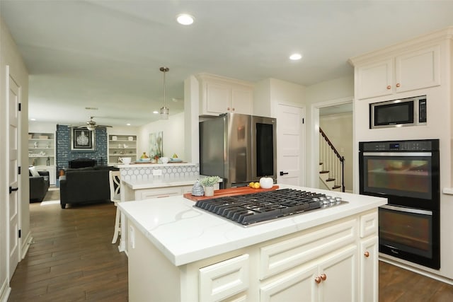 kitchen with dark wood-type flooring, appliances with stainless steel finishes, a center island, a fireplace, and decorative light fixtures