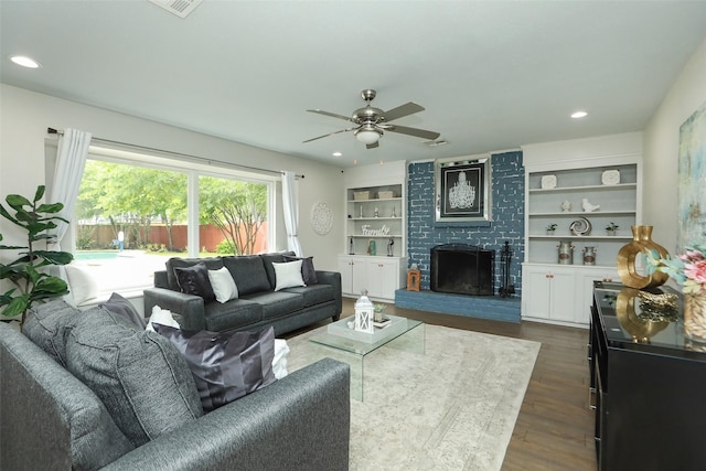 living room with a brick fireplace, dark wood-type flooring, built in features, and ceiling fan