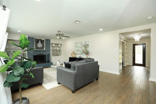 living room featuring hardwood / wood-style flooring, ceiling fan, a fireplace, and built in shelves