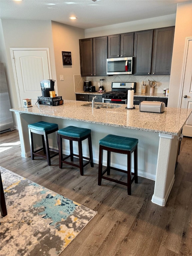 kitchen with a kitchen island with sink, a breakfast bar area, dark hardwood / wood-style floors, dark brown cabinets, and stainless steel appliances