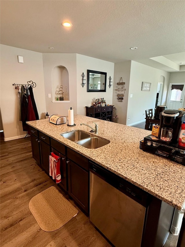 kitchen featuring light stone countertops, dark brown cabinets, a kitchen island with sink, sink, and dishwasher