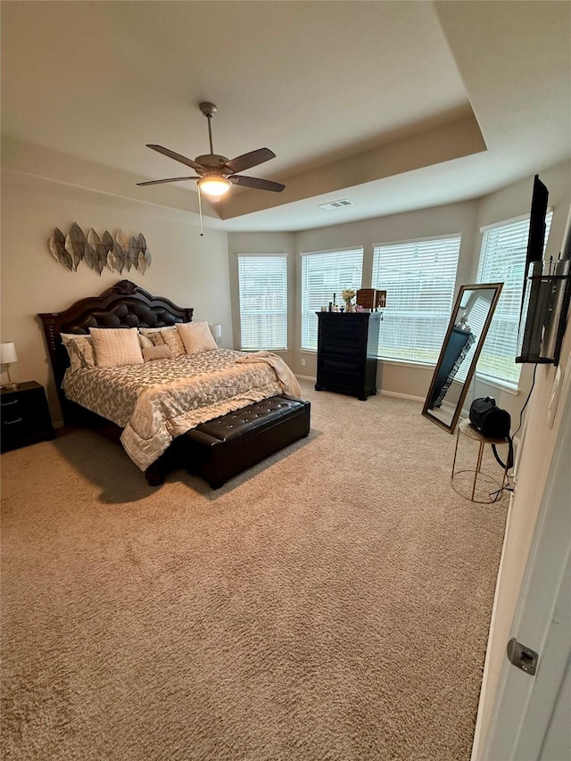 bedroom featuring a raised ceiling, ceiling fan, and light colored carpet