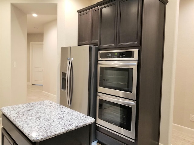 kitchen with a center island, light stone countertops, dark brown cabinetry, and stainless steel appliances