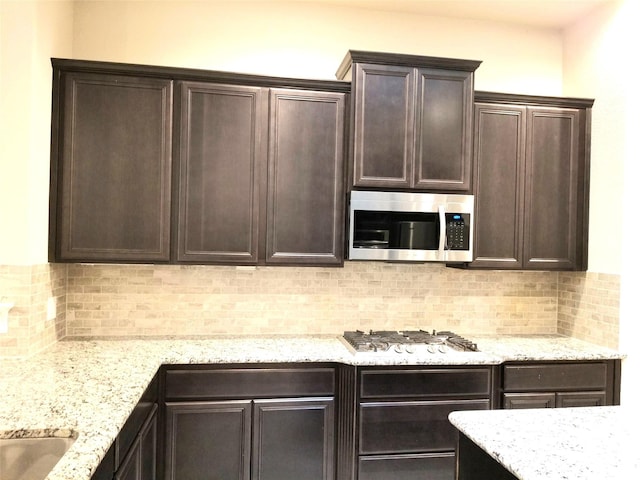 kitchen featuring backsplash, dark brown cabinetry, light stone counters, and stainless steel appliances