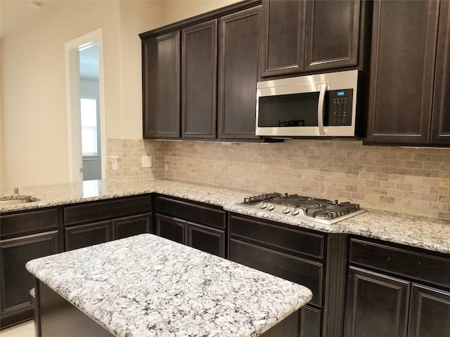 kitchen with light stone countertops, dark brown cabinetry, appliances with stainless steel finishes, and tasteful backsplash