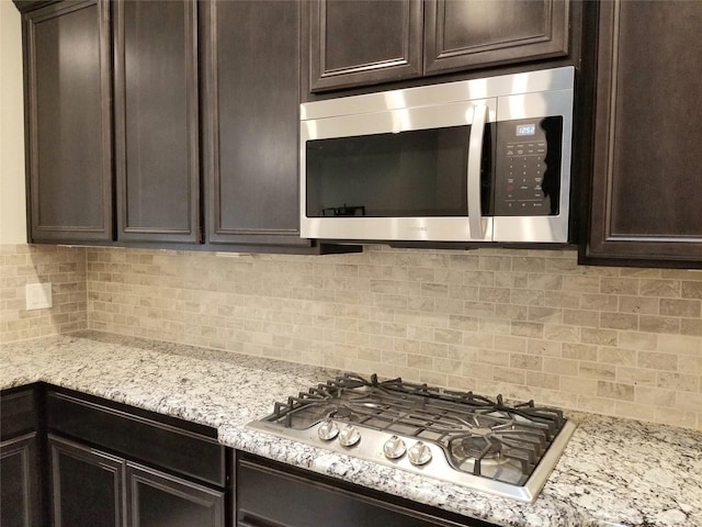 kitchen featuring dark brown cabinets, light stone counters, stainless steel appliances, and tasteful backsplash