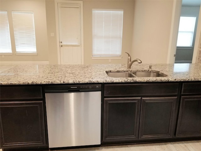 kitchen featuring dishwasher, light stone counters, and sink