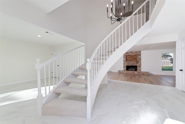 staircase with a notable chandelier and a brick fireplace