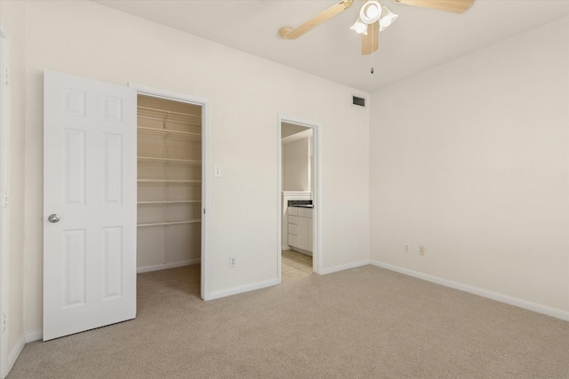 unfurnished bedroom featuring a walk in closet, a closet, ceiling fan, and light colored carpet