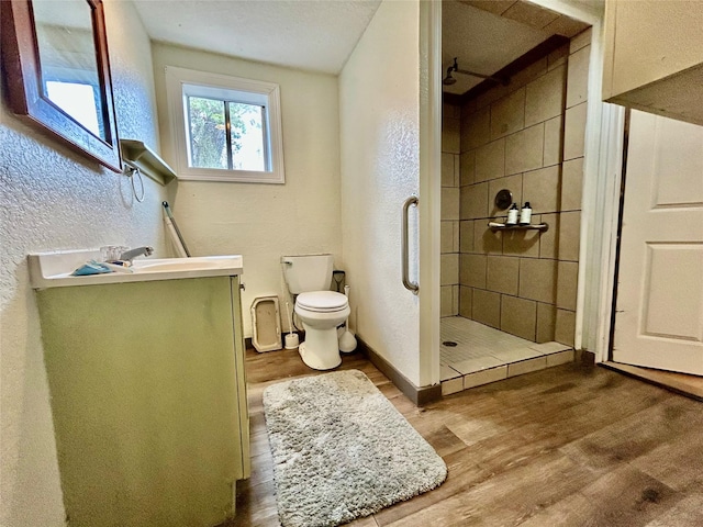 full bath featuring a textured wall, toilet, a stall shower, wood finished floors, and baseboards