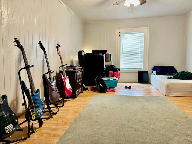 rec room featuring wood walls, ceiling fan, a textured ceiling, and wood finished floors