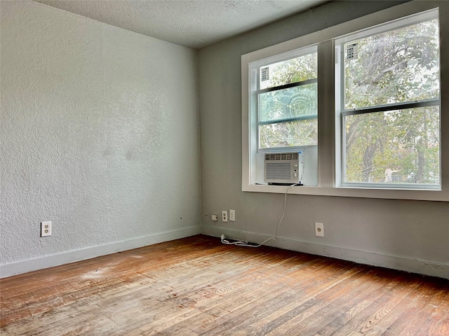 empty room with light wood finished floors, baseboards, a textured ceiling, and a textured wall