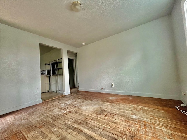 spare room with a textured ceiling, a textured wall, wood-type flooring, and baseboards