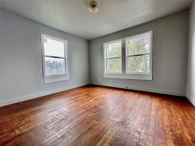 spare room featuring plenty of natural light, wood-type flooring, baseboards, and a textured ceiling