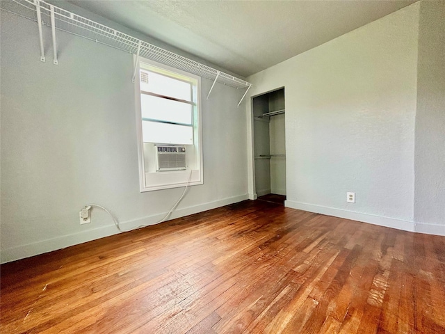 unfurnished bedroom with hardwood / wood-style flooring, a closet, baseboards, and cooling unit