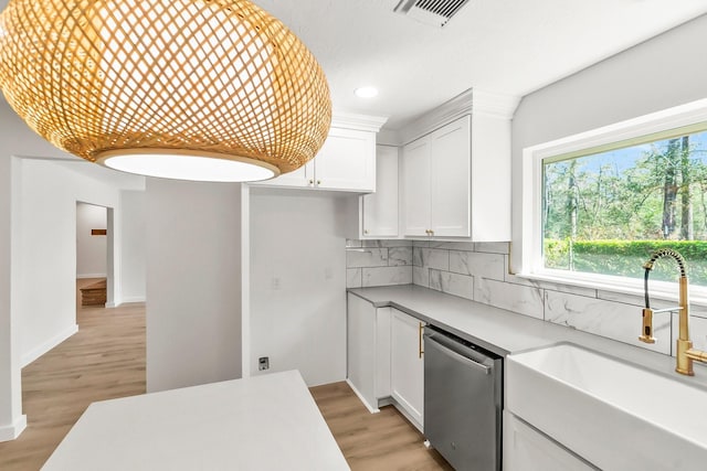 kitchen featuring sink, white cabinetry, light wood-type flooring, stainless steel dishwasher, and backsplash