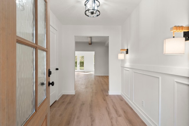 corridor with an inviting chandelier, light hardwood / wood-style floors, and beamed ceiling