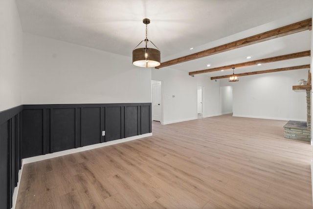 empty room featuring light wood-type flooring, beamed ceiling, and a stone fireplace