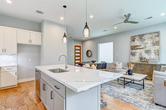 kitchen with dishwasher, a center island with sink, hanging light fixtures, and light stone counters