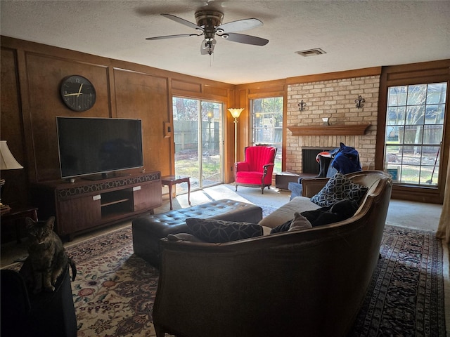 living room featuring ceiling fan, a brick fireplace, wood walls, and a textured ceiling