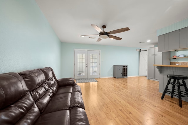 living room featuring french doors, a barn door, light hardwood / wood-style flooring, and ceiling fan