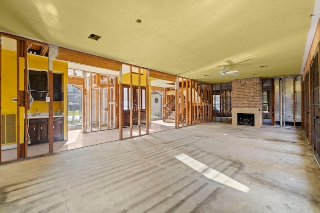 unfurnished living room featuring ceiling fan and a brick fireplace