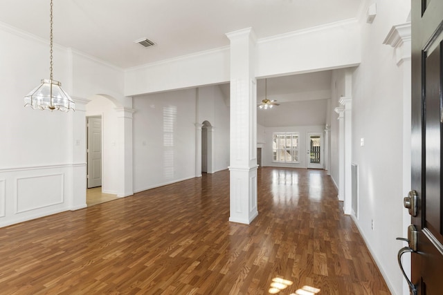 empty room with ceiling fan with notable chandelier, crown molding, dark wood-type flooring, and decorative columns