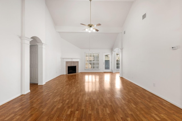 unfurnished living room featuring ceiling fan, wood-type flooring, a tile fireplace, and decorative columns