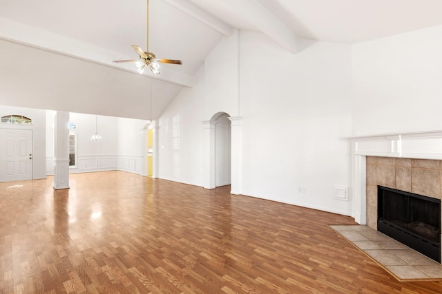 unfurnished living room with high vaulted ceiling, a tile fireplace, hardwood / wood-style flooring, ceiling fan, and beamed ceiling