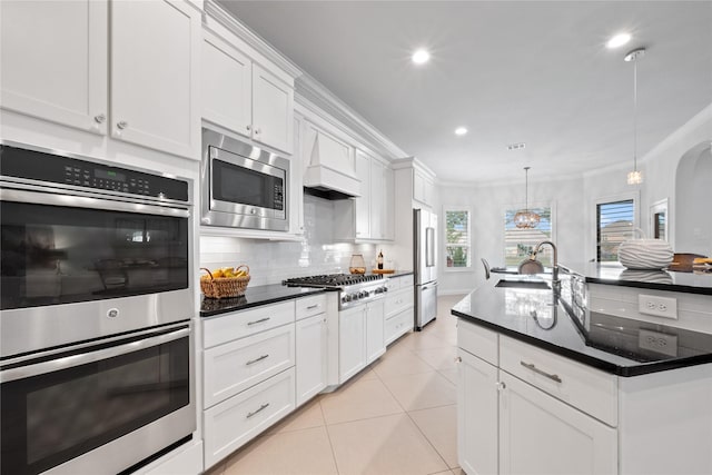 kitchen with white cabinetry, sink, stainless steel appliances, premium range hood, and decorative light fixtures