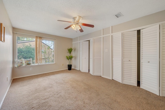 unfurnished bedroom with two closets, ceiling fan, carpet, and a textured ceiling