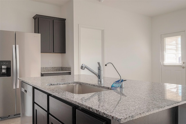 kitchen featuring sink, stainless steel appliances, light stone counters, and an island with sink