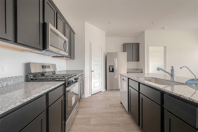 kitchen with light stone countertops, sink, light wood-type flooring, and stainless steel appliances