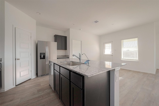 kitchen featuring sink, light stone countertops, light wood-type flooring, an island with sink, and stainless steel appliances